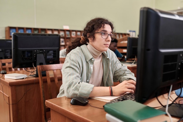 Фото Студент смотрит на экран компьютера в библиотеке