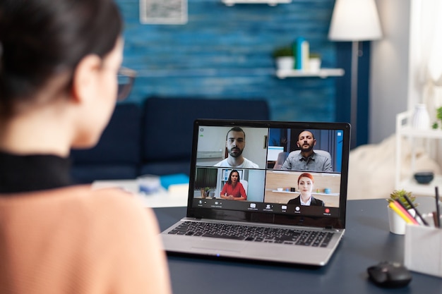 Student luisteren collega's tijdens online videocall schoolvergadering met behulp van laptopcomputer. Jonge vrouw met onderwijs op afstand tijdens quarantaine van het coronavirus terwijl ze in de woonkamer zit