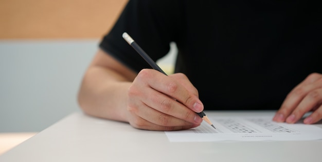 Foto mano dell'uomo dello studente facendo uso della matita per fare esame di testo