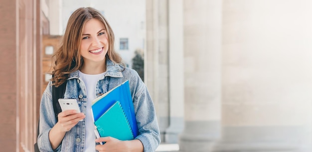 Student meisje glimlachend tegen universiteit houdt mappen notebooks en mobiele telefoon webbanner