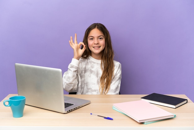 Student meisje op een werkplek met een laptop geïsoleerd op een paarse achtergrond met ok teken met vingers