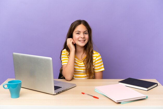 Student meisje op een werkplek met een laptop geïsoleerd op paarse achtergrond lachen