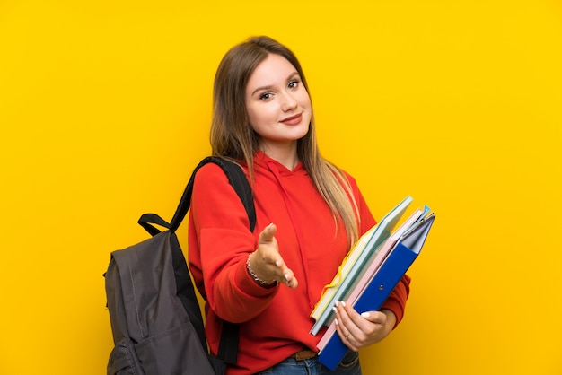 Student meisje over gele muur handshaking na goede deal