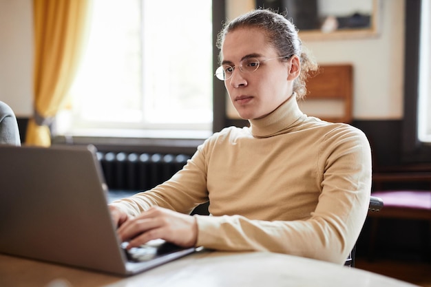 Student met bril die zich concentreert op zijn online werk op laptop aan tafel