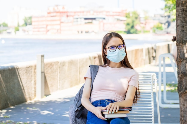 Student met een masker en een bril met boeken in de buurt van de universiteit die tieners lesgeeft tijdens de covid19 pandemische bescherming tegen het coronavirus