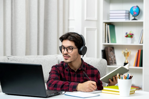 Studente online ragazzo carino in camicia a quadri con gli occhiali che studia sul computer ascoltando l'insegnante