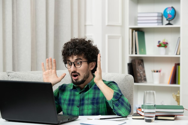 녹색 셔츠에 안경을 쓰고 컴퓨터에서 공부하는 온라인 귀여운 젊은 남자가 손을 흔들며 혼란스러워한다