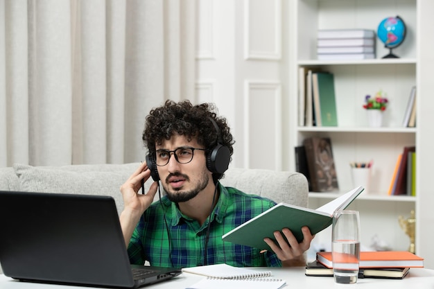 Student online schattige jonge kerel die op de computer studeert in een bril in een groen shirt, denkend en gefocust