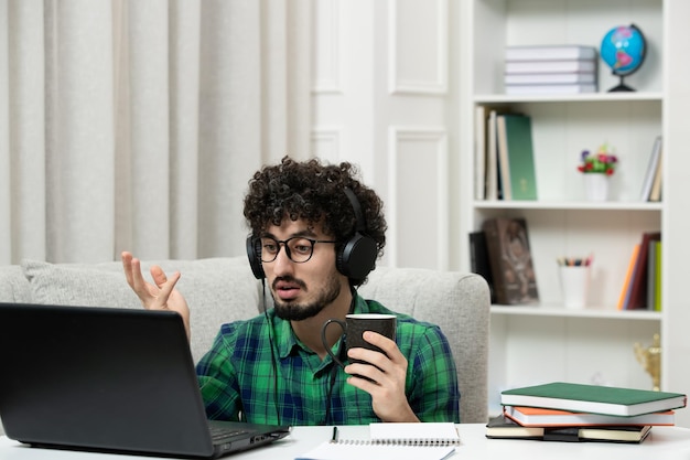 Student online schattige jonge kerel studeren op computer in glazen groen shirt zwaaiende handen verwarrend