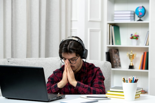 Student online schattige kerel in geruit overhemd met bril die op computer studeert en biddend teken maakt