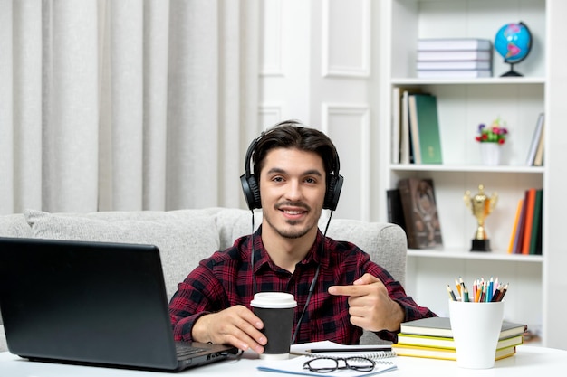 Student online schattige kerel in geruit overhemd met bril studeren op computer met een papieren bekertje