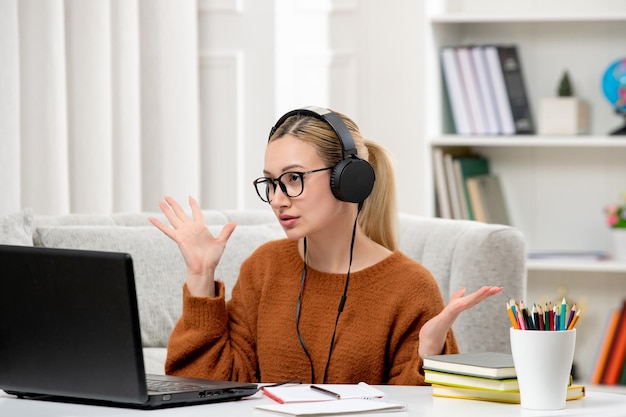 Photo student online young cute girl in glasses and orange sweater studying on computer confused