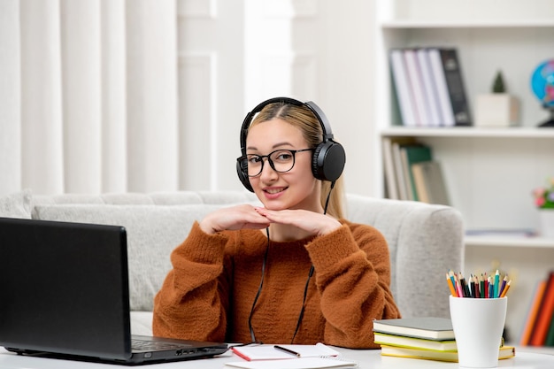 Student online young cute girl in glasses and orange sweater studying on computer holding hands