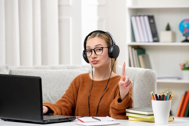 Student online young cute girl in glasses and orange sweater studying on computer showing stop sign