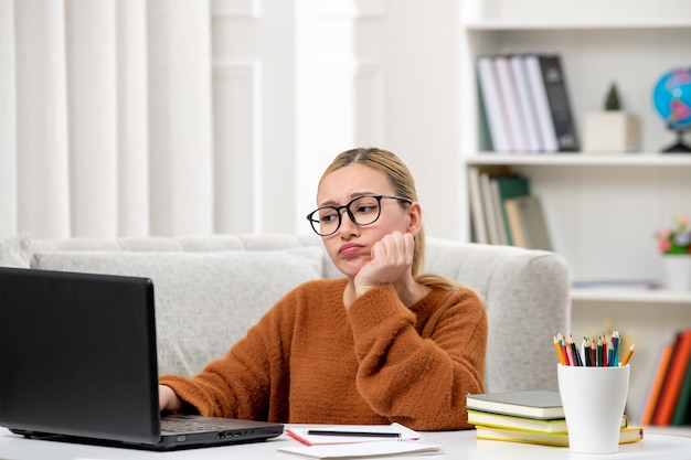 Student online young cute girl in glasses and orange sweater studying on computer tired