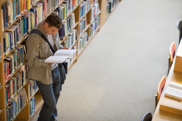 Student reading a book from shelf standing in library 