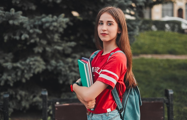 A student in a red T-shirt with a backpack and colored notebooks on the street