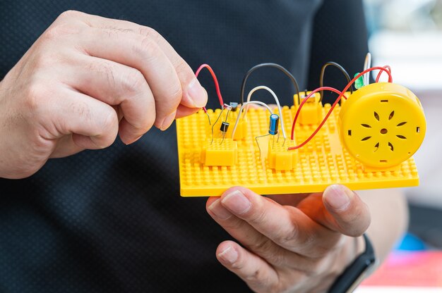 Foto la mano dello studente che tiene un kit di invenzione e collega i cavi elettrici.