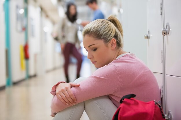 Student sitting on the floor at the hallway looking disappointed