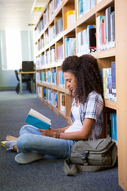 Student sitting on floor in library reading 