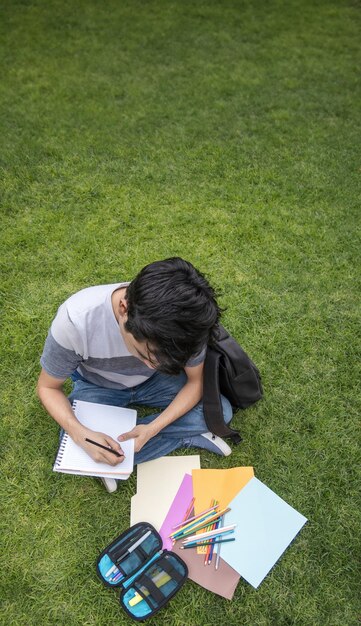 A student sitting on the grass writing in a notebook