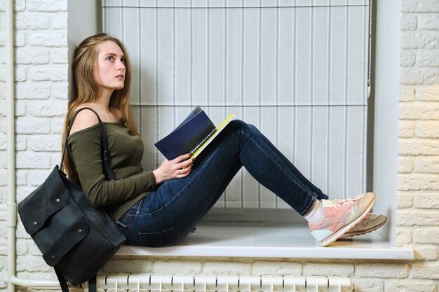 Student sitting on windowsill, studying, reading notebook