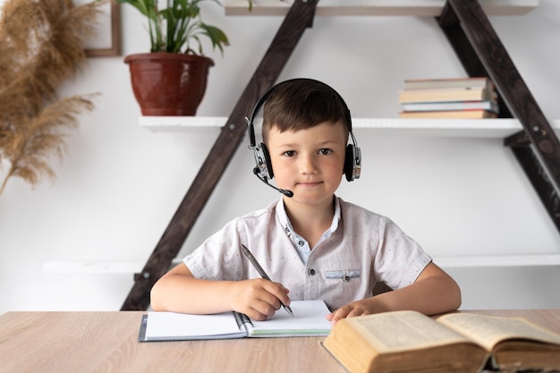 A student sitting with headphones at a desk listens to the teacher and writes homework in a notebook Online education or tutor Home lesson for a student Wireless headset