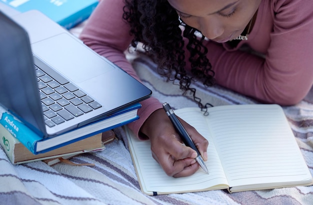 Student studying and woman writing notes from research assignment for college or university academic education Park learning and African American young female Elearning or remote with a textbook