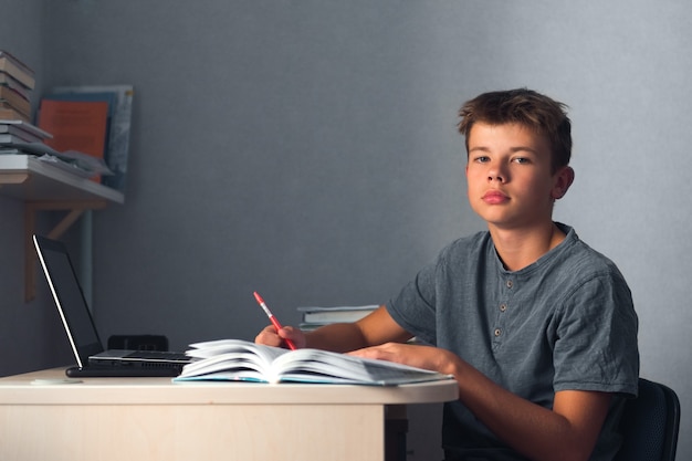 Foto ragazzo dell'adolescente dello studente che fa i compiti con il quaderno aperto del computer portatile e il posto di lavoro del computer a casa