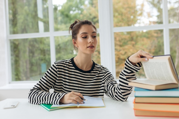 Student thuis leren van boeken Jong meisje zittend op een bureau thuis schrijven in werkboek lezen van boek lachend