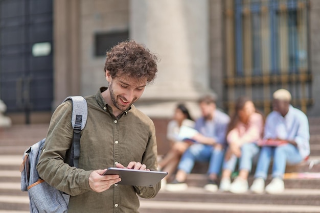 写真 大学の前に立ってデジタル タブレットを使用している学生