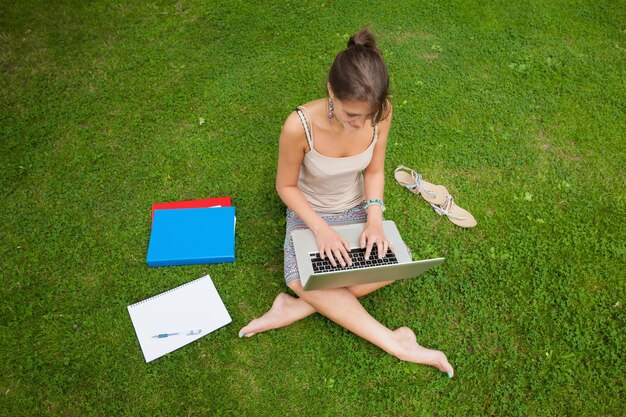 Student using laptop with books at the park