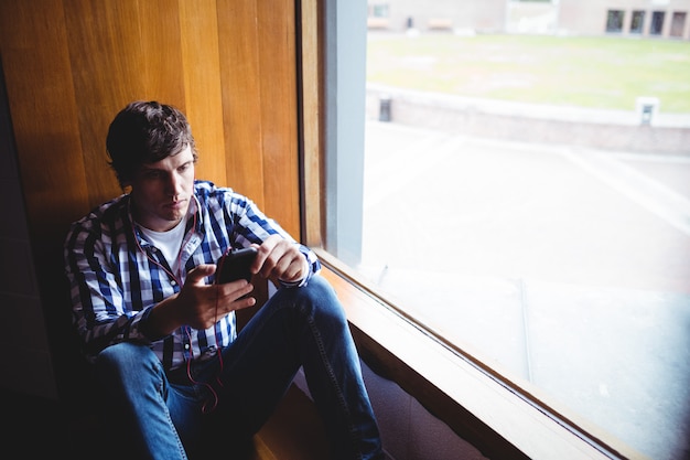 Student using mobile phone near window