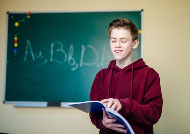 Student van hogere school staat in donkere hoodie dichtbij het groene schoolbord.