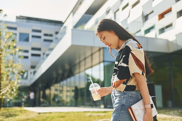 学生は近代的な建物の近くを歩く若いアジアの女性は日中に屋外にいます