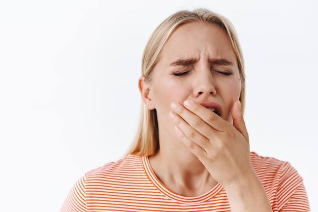 Student werkte hard en voelde vermoeidheid Leuke jonge moderne blonde blanke vrouw moe staande witte achtergrond sluit ogen en opende mond geeuwen wil slaap behoefte ochtend slokje koffie