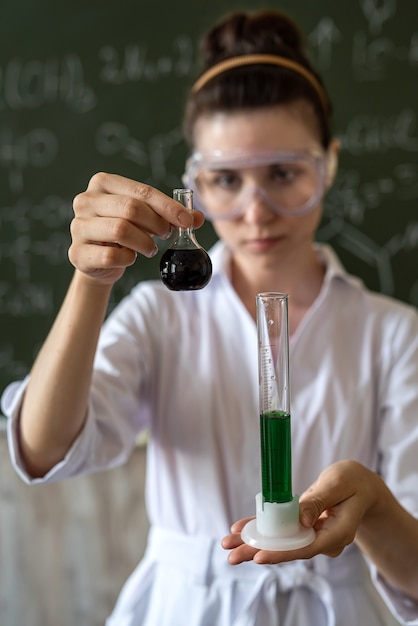 Foto studente in camice bianco e occhiali tiene in mano una fiaschetta e conduce un esperimento, un'università di concetto di educazione