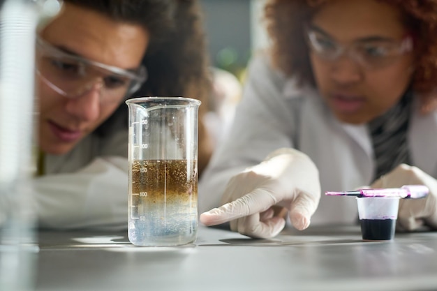 Student wijst naar glas met chemische oplosser tijdens experiment