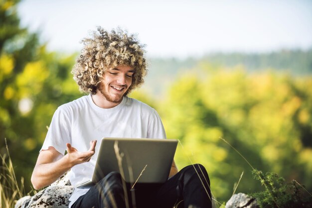 A student with an afro hairstyle sitting in nature and uses a laptop during a corona virus pandemic