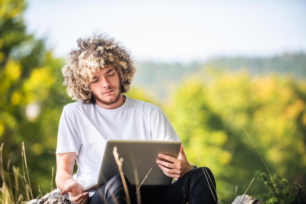 A student with an afro hairstyle sitting in nature and uses a laptop during a corona virus pandemic