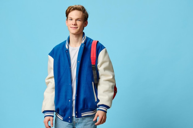 Student with a backpack on his shoulder posing on a blue background