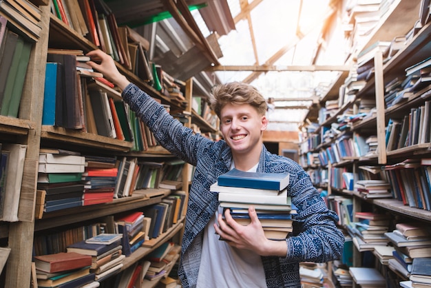 Student with a lot of books in his hands is in the library