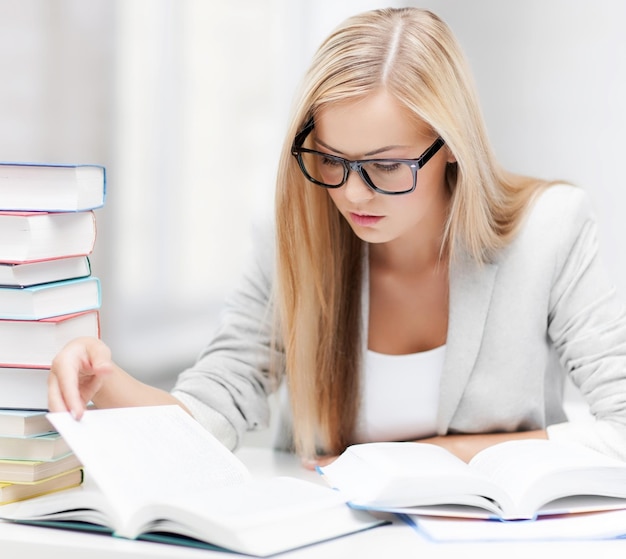 Studente con pila di libri e appunti che studia al chiuso