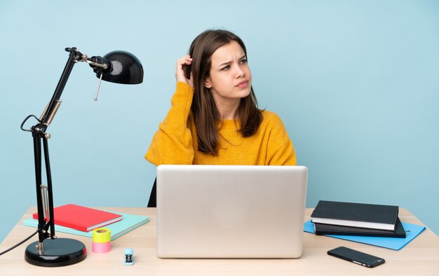 疑問を持つ青い壁に分離された彼女の家で勉強している学生女性