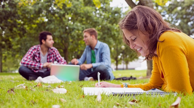 Photo student writing notes with males using laptop at park