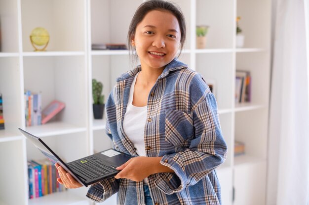 Student young girl hold laptop on bookcase backgroundAsian girl