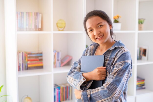 学生の若い女の子は本棚の背景にラップトップを保持しますアジアの女の子