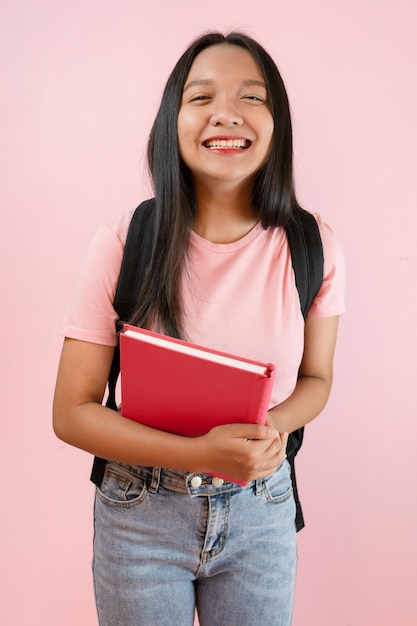 ピンクの背景に本とバックパックを持つ学生の若い女の子