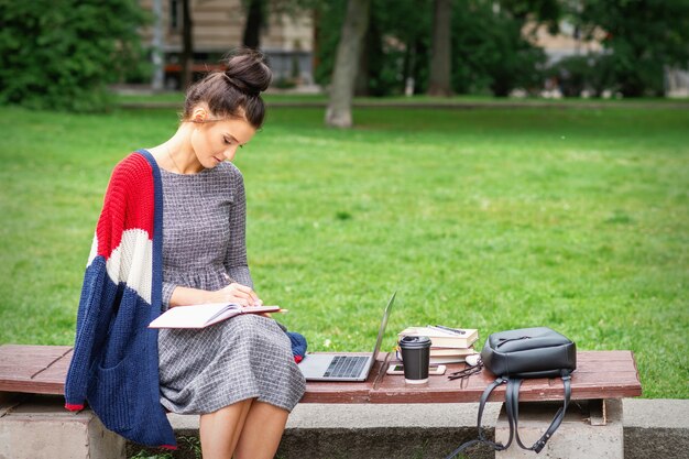 Student young woman is writing notes to diary on the bench in the park