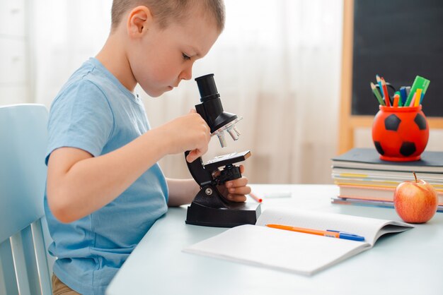 Student zit tafel en bezig met educatief materiaal. schoolkind kijkt door een microscoop.